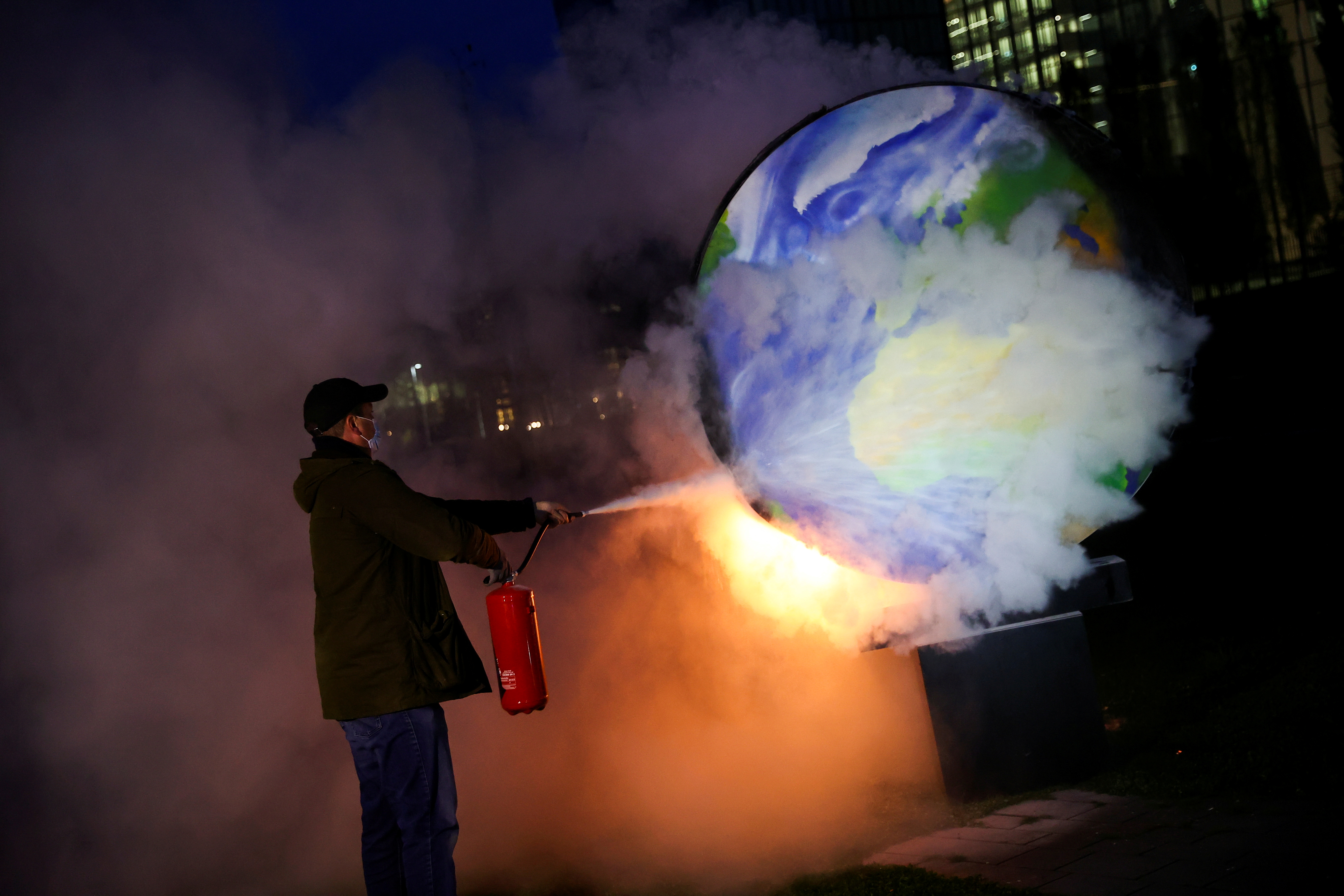 A person uses an extinguisher toward a burning paper-made globe during a demonstration against the fossil fuel industry in Frankfurt, Germany on October 21, 2020. 
