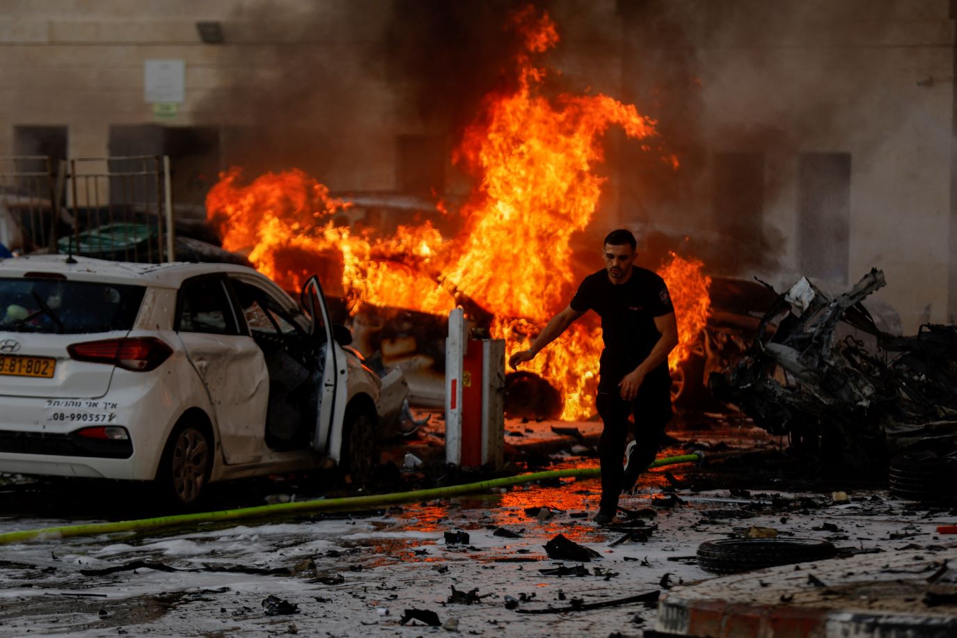A man runs on a road as fire intensely burns from two demolished cars on a debris covered street after rockets were launched from the Gaza Strip, in Ashkelon, Israel on October 7, 2023. 