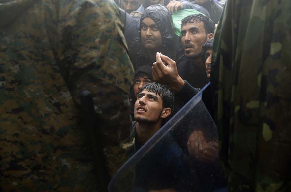 Migrants and refugees beg Macedonian policemen to allow passage to cross the border from Greece into Macedonia during a rainstorm, near the Greek village of Idomeni, September 10, 2015 (Yannis Behrakis/Courtesy Reuters).