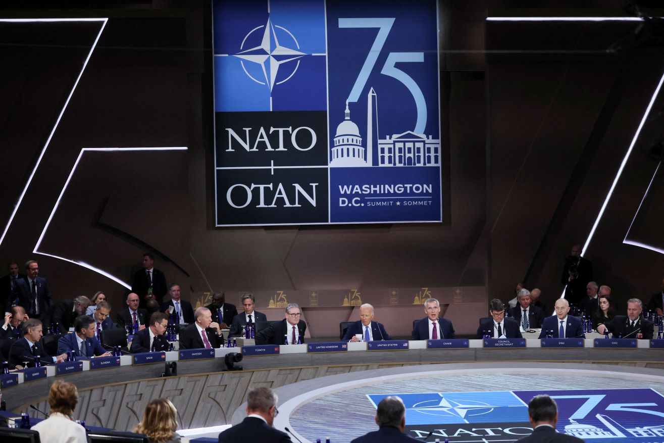Leaders attend a meeting of the North Atlantic Council at a huge roundtable in a dark room with banners on the wall during the NATO summit in Washington, DC, on July 11, 2024. 